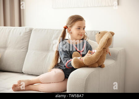 Adorabile bambina esaminando bunny giocattolo con uno stetoscopio a casa Foto Stock