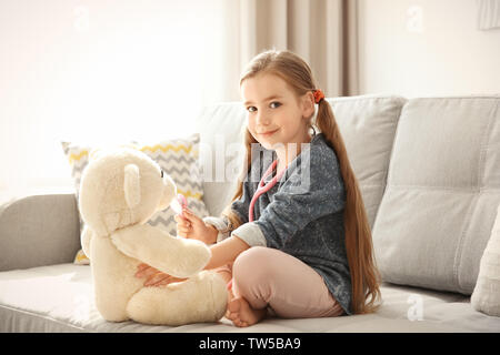 Adorabile bambina esaminando orsacchiotto con uno stetoscopio a casa Foto Stock