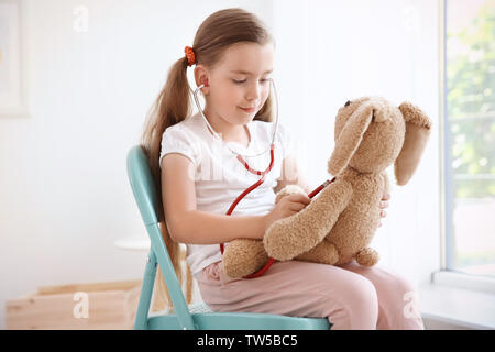 Adorabile bambina esaminando bunny giocattolo con uno stetoscopio a casa Foto Stock