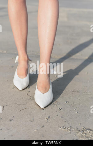 Scarpe bianche sulla ragazza in piedi. Le gambe nelle scarpe sono close-up. Una ragazza in scarpe alla moda passeggiate attraverso la citta'. Asfalto al calpestio. Ph verticale Foto Stock