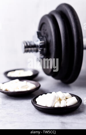 La creatina, taurina, Beta alanina di capsule e di un manubrio. Bodybuilding integratori alimentari su un sfondo di pietra. Close up. Copia dello spazio. Foto Stock