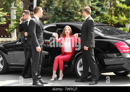 Guardie del corpo aiutando giovane imprenditrice per uscire dall'auto Foto Stock