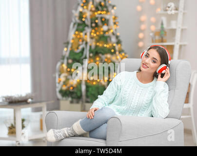 Bella giovane donna ascoltando musica in salotto decorato per il Natale Foto Stock