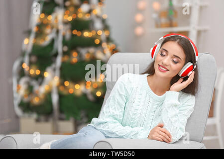 Bella giovane donna ascoltando musica in salotto decorato per il Natale Foto Stock