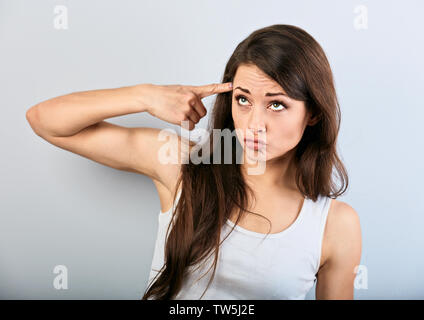 Giovane ragazza beauiful mostrando dito gesto pistola, tiro se stessa e cercando su sfondo blu. Primo piano Foto Stock