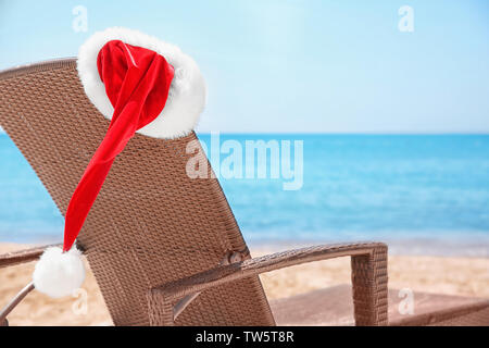 Vuoto lettino con Santa hat sulla spiaggia vicino al mare. Vacanze di Natale del concetto Foto Stock