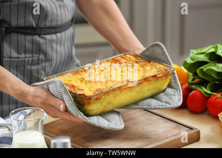 Donna che mantiene la griglia da forno con spinaci lasagne in cucina Foto Stock