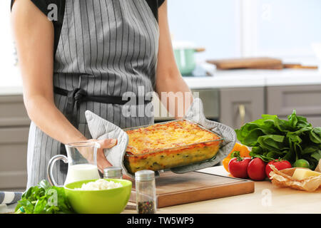 Donna che mantiene la griglia da forno con spinaci lasagne in cucina Foto Stock