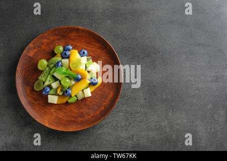 Piastra con una deliziosa insalata di frutta su sfondo scuro Foto Stock