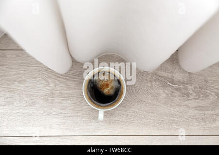 Tazza di caffè sul pavimento vicino a tendaggi Foto Stock