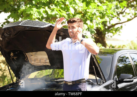 Uomo che parla al telefono vicino a Broken auto sulla strada Foto Stock