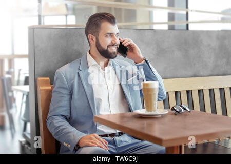Bel imprenditore di successo parlando al telefono cellulare in cafe Foto Stock