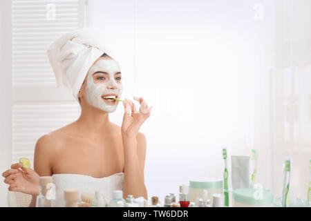 Giovane donna con maschera al viso e fette di cetriolo in bagno Foto Stock