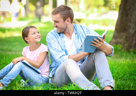 Il giovane e la sua piccola figlia la lettura di libri in posizione di parcheggio Foto Stock