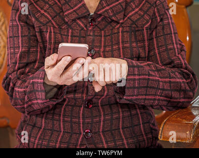 Asian anziani donna seduta e guardando attraverso qualcosa su smartphone moderno, effettua il collegamento con altri utenti a casa, vivere la tecnologia, close up Foto Stock