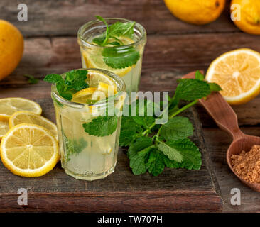 Estate bevanda rinfrescante limonata con limoni, foglie di menta in un bicchiere, accanto agli ingredienti per la realizzazione di un cocktail Foto Stock