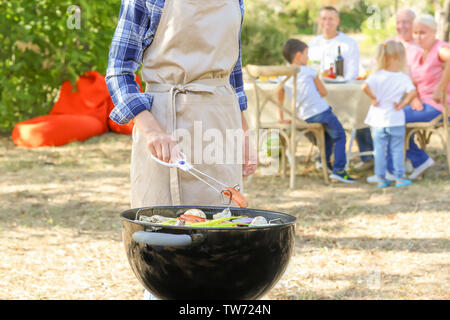 La donna la cottura di gustose salsicce con verdure su barbecue grill all'aperto Foto Stock