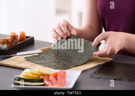 Giovane donna rendendo rotoli di sushi a casa Foto Stock