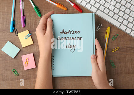 Donna che mantiene un notebook con parole scritte "Autismo consapevolezza giorno' sulla tabella Foto Stock