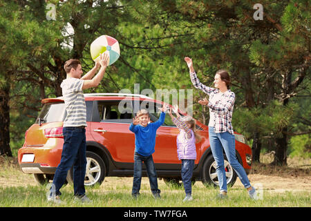 La famiglia felice giocando con la palla vicino auto moderna all'aperto Foto Stock