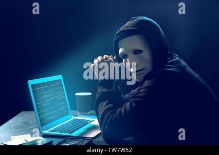 Hacker in maschera con il computer portatile in camera oscura Foto Stock