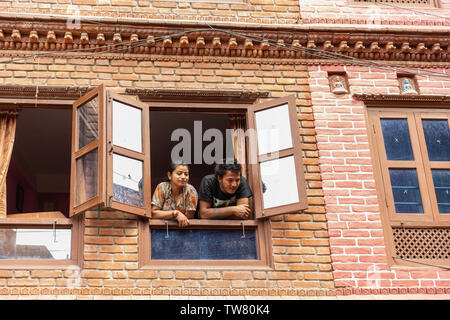 Coppia giovane guardando fuori da una finestra al piano di sopra, Bhaktapur, Provincia n. 3, Nepal, Asia Foto Stock