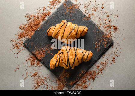 Piastra di ardesia con gustosi croissant su sfondo grigio Foto Stock