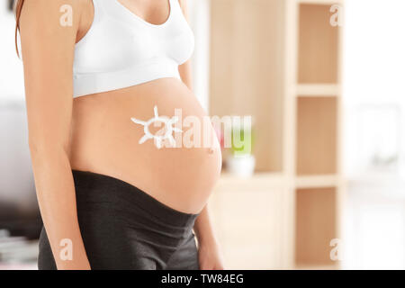 Sun dipinta con crema sulla donna incinta il ventre contro sfondo sfocato Foto Stock