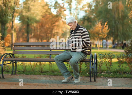 Elegante uomo maturo con fotocamera seduta sul banco in autunno park Foto Stock