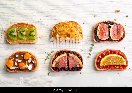 Fette di pane con vari condimenti su sfondo chiaro Foto Stock