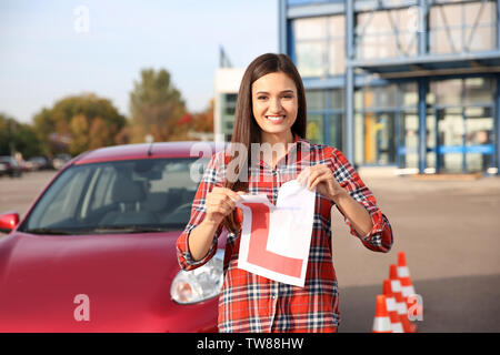 Felice giovane donna strappo allievo conducente segno vicino auto Foto Stock