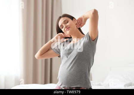 Giovane donna incinta lo stiramento su letto di casa Foto Stock