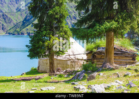 In estate, le case di legno di pastori kazake sono ricoperte di erba sul bordo di Tianchi in montagna Tianshan Foto Stock