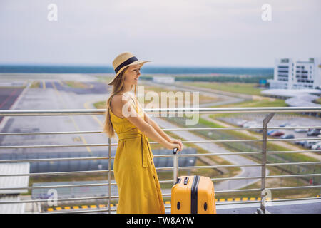 Inizio del suo cammino. Bella giovane donna ltraveler in un abito giallo e una valigia di colore giallo è in attesa per il suo volo Foto Stock