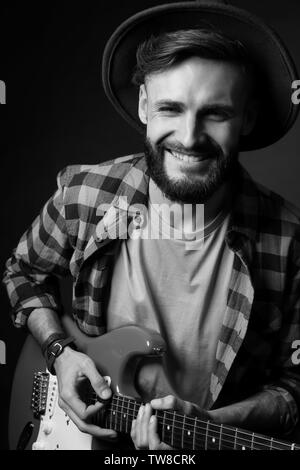 Giovane musicista bello suonare la chitarra su sfondo nero Foto Stock