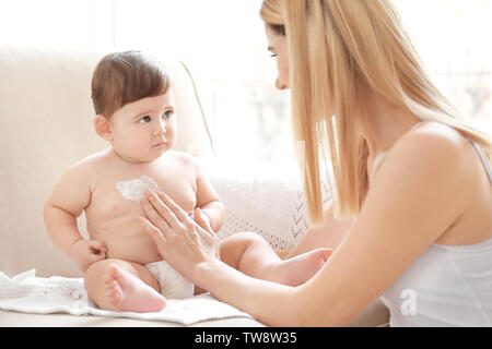 Donna l'applicazione di crema per il corpo sul suo bambino in ambienti interni Foto Stock