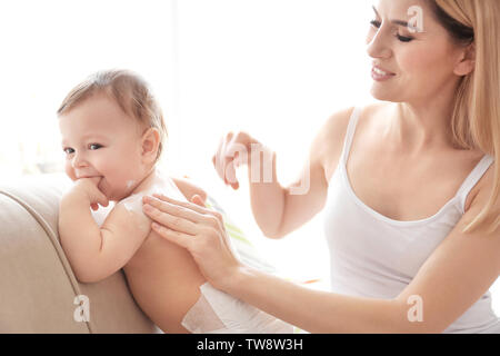 Donna l'applicazione di crema per il corpo sul suo bambino in ambienti interni Foto Stock