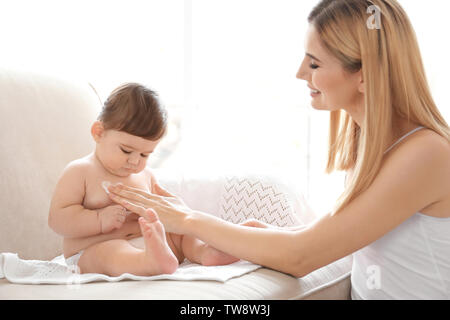 Donna l'applicazione di crema per il corpo sul suo bambino in ambienti interni Foto Stock