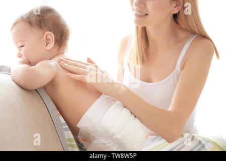 Donna l'applicazione di crema per il corpo sul suo bambino in ambienti interni Foto Stock