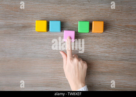 Donna messa ultimo color cube in fila sullo sfondo di legno. Il concetto di unità Foto Stock