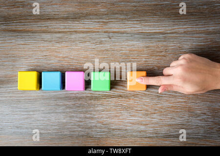 Donna messa ultimo color cube in fila sullo sfondo di legno. Il concetto di unità Foto Stock