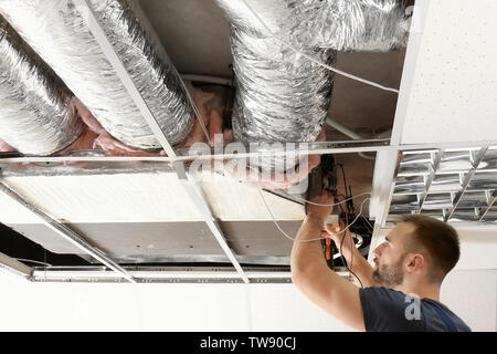 Tecnico maschio misura la tensione durante la riparazione industriale di un condizionatore di aria in ambienti interni Foto Stock