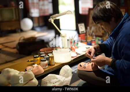 Artigiano giapponese rendendo Hyottoko, carattere comico, festival maschere nella sua bottega. Ainokura, Toyama, Giappone. Foto Stock