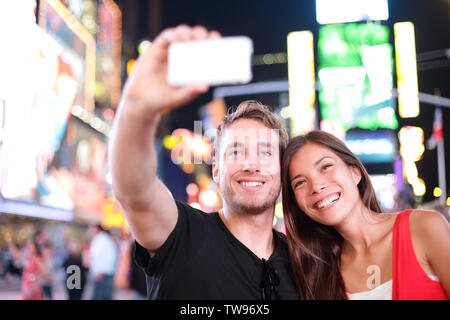 Dating coppia giovane felice in amore tenendo selfie Self-portrait foto su Times Square di New York City di notte. Bella giovani turisti divertendosi data, Manhattan STATI UNITI D'AMERICA. Donna asiatica, uomo caucasico Foto Stock