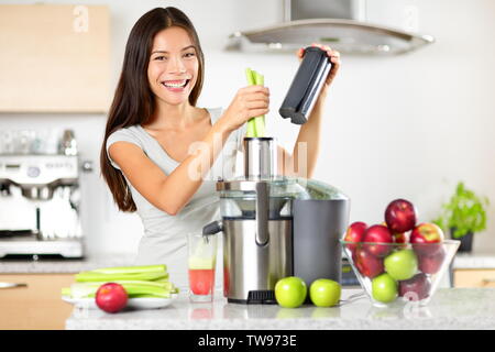 Un succo vegetale materie alimentari - mangiare sano donna con centrifuga a spremere il succo di verdura verde e frutti di Apple come parte del suo benessere alimentare. Bella felice mescolato donna asiatica con succo maker in cucina. Foto Stock