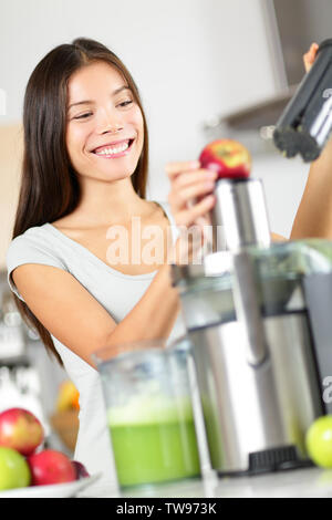 Donna che rendono Apple e un succo vegetale sulla macchina centrifuga a casa in cucina. Spremere il succo e mangiare sano donna felice realizzazione di verdura verde e succo di frutta. Gara di Misto Asiatico modello caucasico. Foto Stock