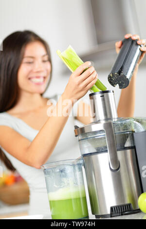 Succo di verdura - donna a spremere il succo di verdura verde sulla macchina centrifuga o creatore di succo. Un sano cibo crudo concetto con la persona che effettua il sedano succo di verdura in cucina. Focus sul sedano. Foto Stock