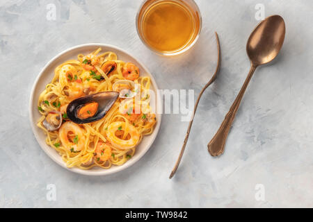 Piatti di pasta, overhead closeup shot. Tagliolini con cozze, gamberi, vongole e anelli di totano, con un bicchiere di vino bianco Foto Stock