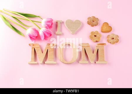 La frase "Io amo mamma' fatto di lettere di legno e fiori con i cookie sul colore di sfondo. Auguri per la festa della mamma Foto Stock