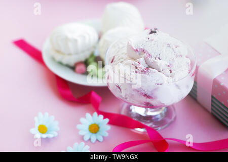 Berry ice cream in vetro ciotola da dessert su sfondo sfocato con doni, dolci, sfondo rosa, il fuoco selettivo, le sfocature Foto Stock